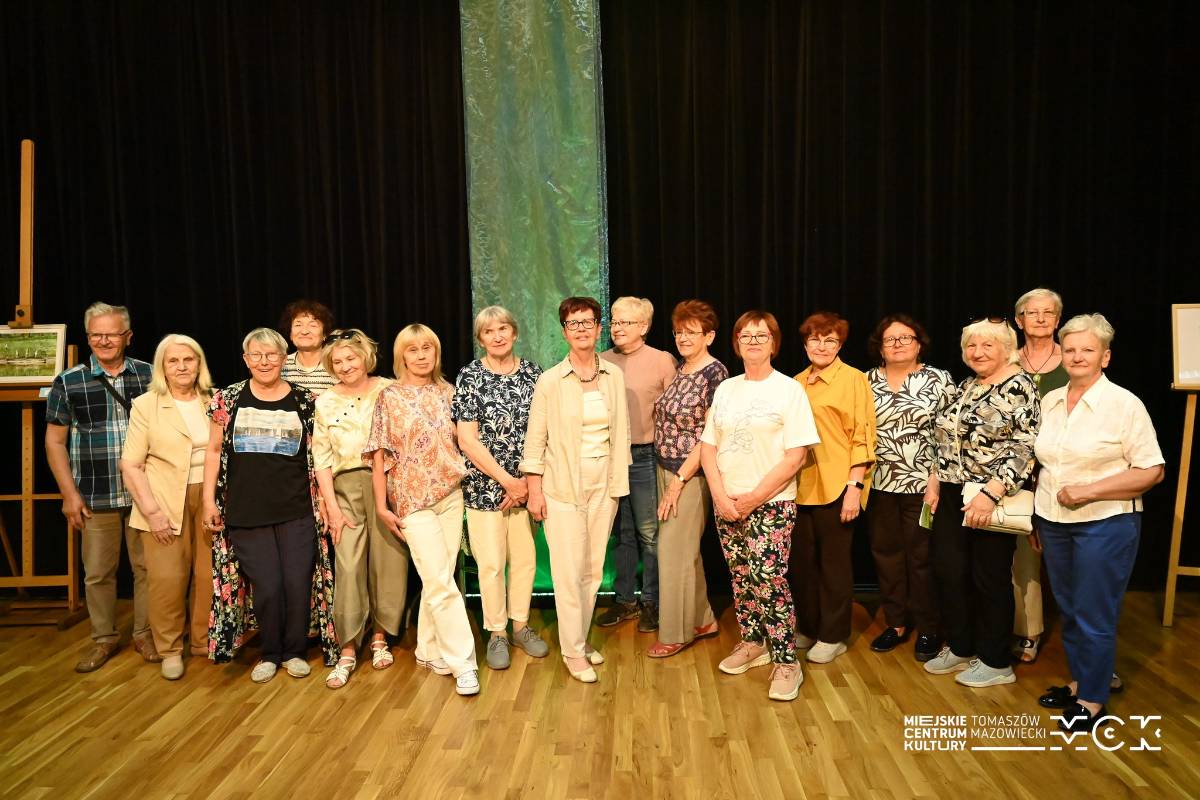 Na zdjęciu artyści-seniorzy wystawiający swoje prace podczas wernisażu w Miejskim Centrum Kultury Tkacz. Pozują na scenie, zdjęcie grupowe
