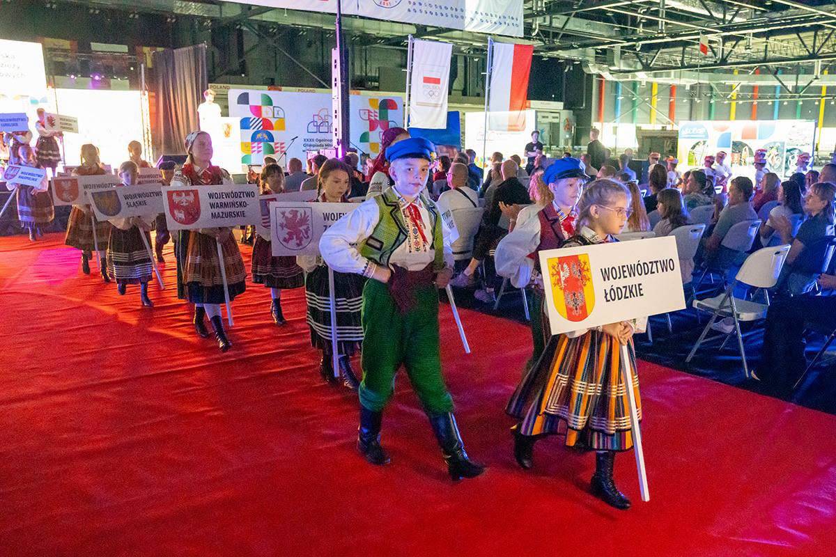 Na zdjęciu dzieci w strojach ludowych niosą tabliczkę z napisem województwo łódzkie podczas ceremonii zakończenia XXXII Ogólnopolskiej Olimpiady Młodzieży w Sportach Halowych Łódzkie 2026