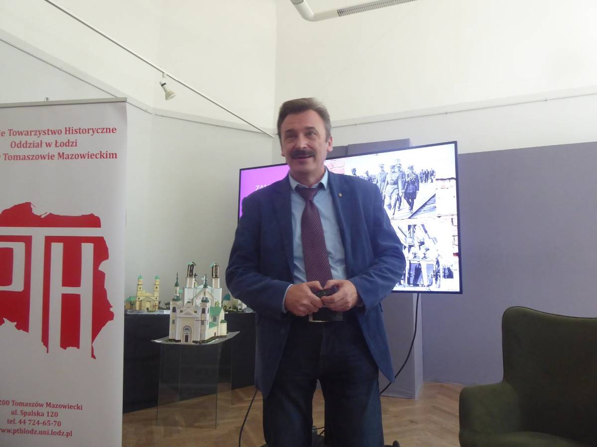 Wykład w muzeum o przewrocie majowym 1926 roku w Muzeum. Prowadzący wykład stoi na tle ekranu, na którym wyświetlona jest grafika historyczna
