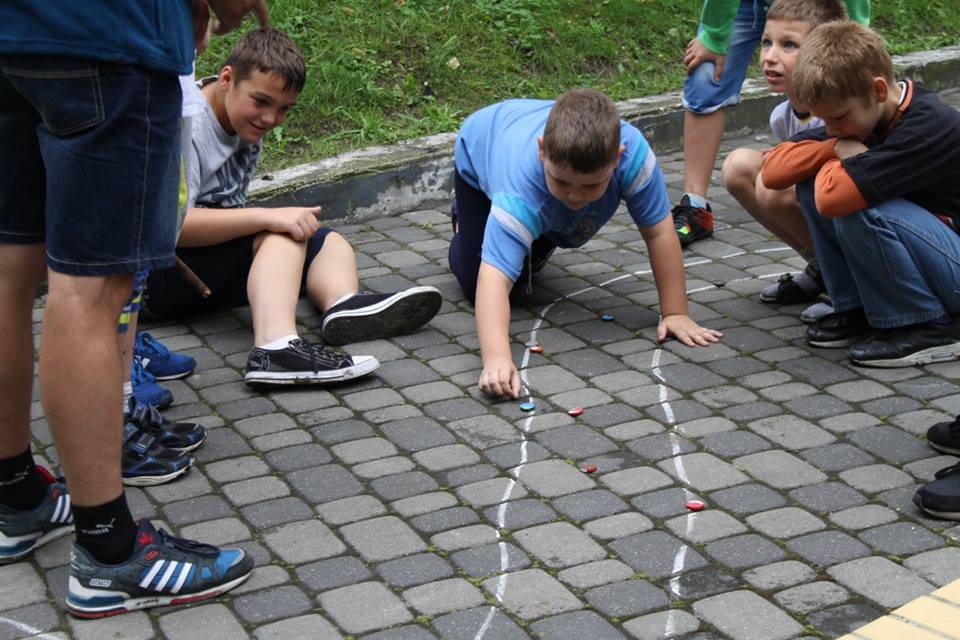 Na zdjęciu grupa chłopców w gra kapslami w kolaże. Trasa wyrysowana na kostce brukowej