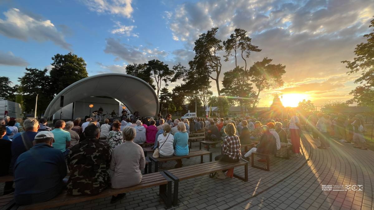 Na zdjęciu koncert Kapeli Spalskiej podczas Letniej Sceny Artystycznej. Widać publiczność oglądającą występ kapeli w amfiteatrze na Przystani nad Pilicą. Zapada wieczór