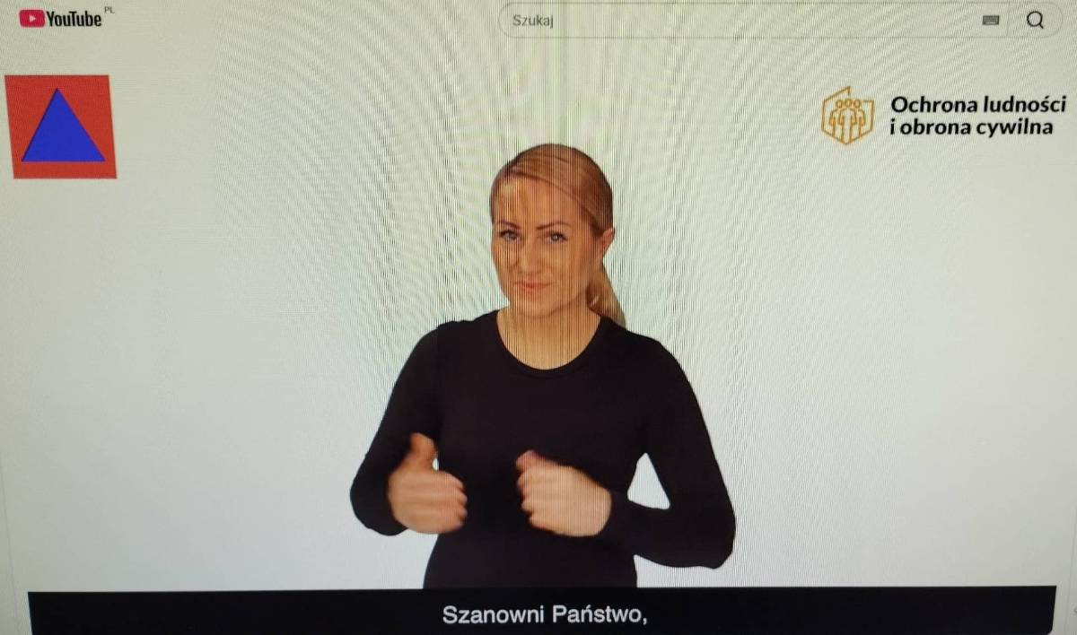 Na zdjęciu kadr z Poradnika bezpieczeństwa na You Tube przetłumaczonego na język migowy . W kadrze lektorka w czarnym kostiumie tłumaczy tekst poradnika.