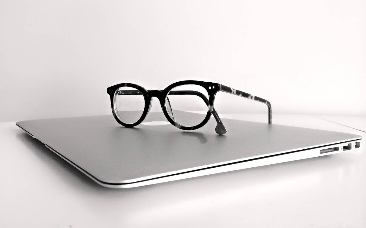 Na zdjęciu okulary w oprawkach leżą na pulpicie zamkniętego laptopa