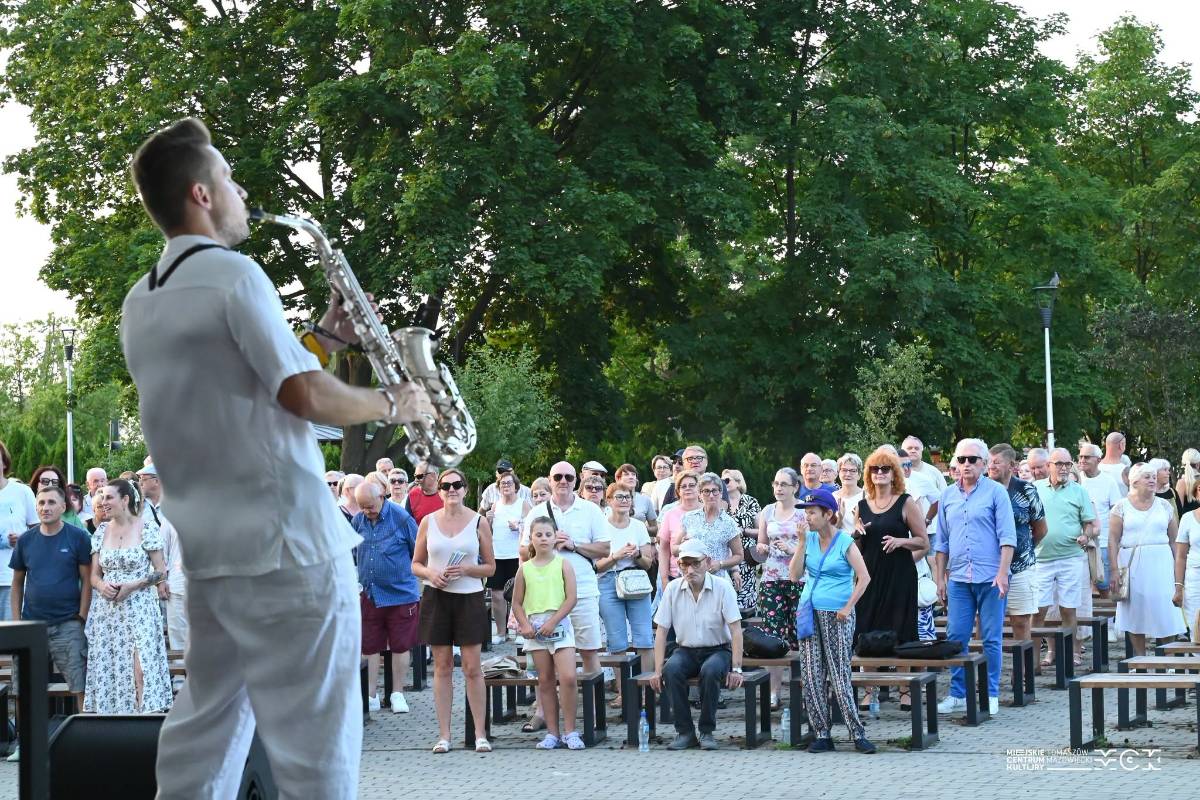 Na zdjęciu saksofonista Dave Bo gra na saksofonie stojąc na deskach amfiteatru na Przystani nad Pilicą. Publiczność zgromadzona na koncercie wstała z ławek i słucha