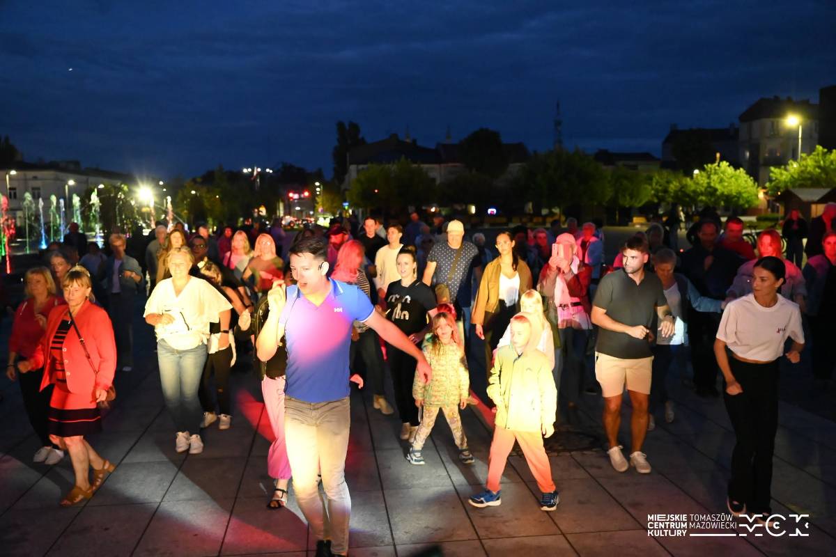 Na zdjęciu już podczas wieczoru Tomaszowianie pod przewodnictwem DJ i tancerzy uczestniczą w potańcówce na Placu Kościuszki. Widać tłum mieszkańców w różnym wieku, tańczą w rytm muzyki i kolorowych świateł