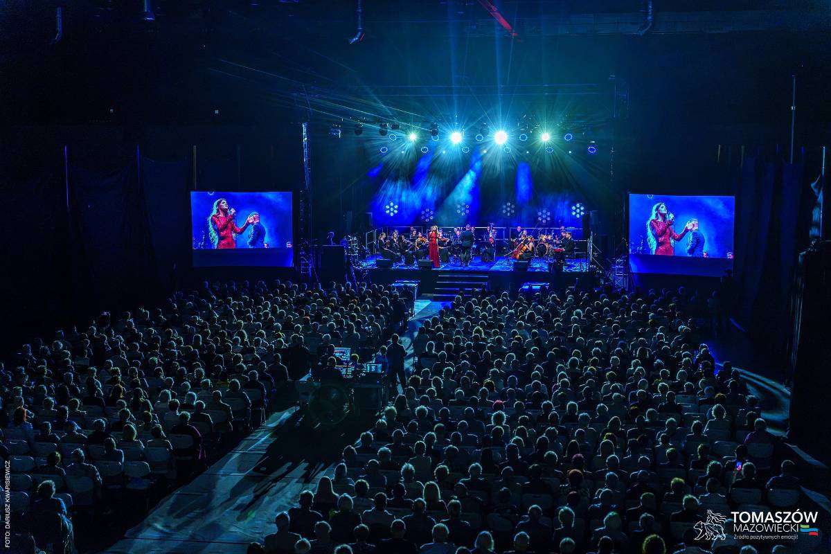 Sala widowiskowa, tłum ludzi, scena osnuta granatowym światłem, na niej artyści