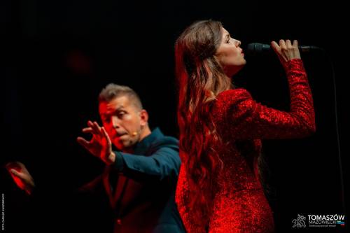 Koncert Katarzyny Zawady z TM Orchestra. N scenie wokalistka odwrócona tyłem do publiczności śpiewa do mikrofonu. Ma na sobie długą, czerwoną suknię. Obok stoi dyrygent Tomaszowskiej Orkiestry Symfonicznej i  żywo gestykuluje