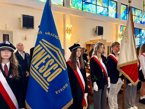 Poczty sztandarowe w kościele pw. NMP Królowej Polski przy ul. Słowackiego. Młodzież w galowych strojach i biało-czerwonych szarfach asystuje, trzyma sztandary na drzewcach. W tle uczestnicy obchodów
