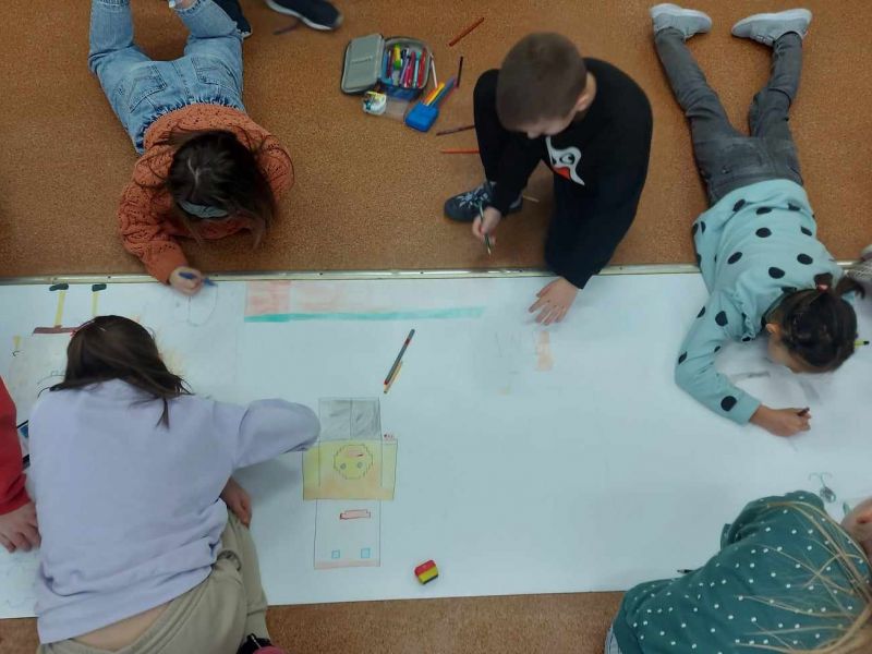 Na zdjęciu uczestnicy zajęc feryjnych w szkołach rysują na rozwiniętym rulonie papieru