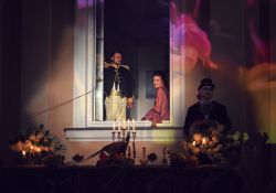 Na zdjęciu kadr ze spektaklu u Hrabiego. Aktorzy grający małżeństwo hrabiów Ostrowskich gra w otwartym oknie pałacu ostrowskich. Przed oknem zastawiony stół i lokaj
